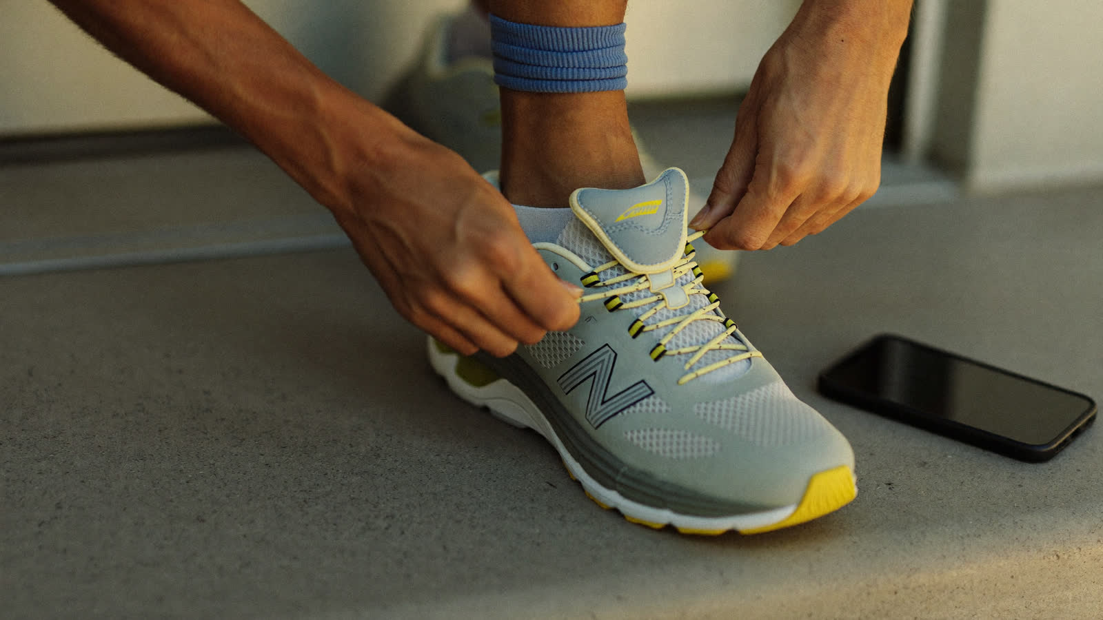 Hands lacing a running shoe at dawn, a phone resting beside
