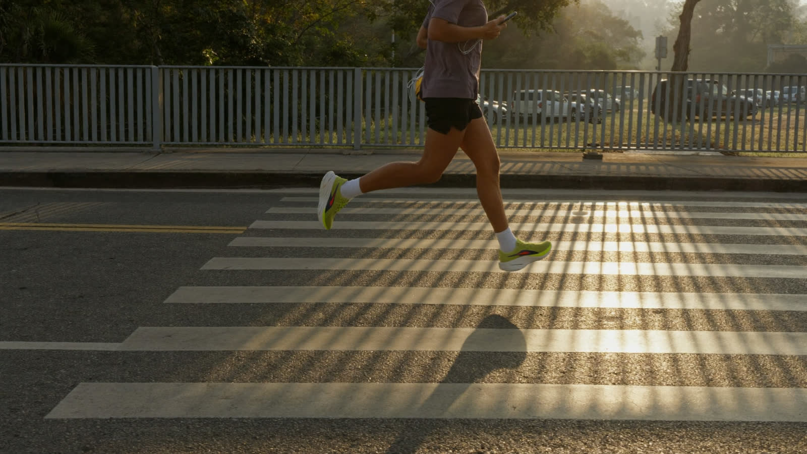 A runner mid-stride on a bridge at sunrise, phone in hand